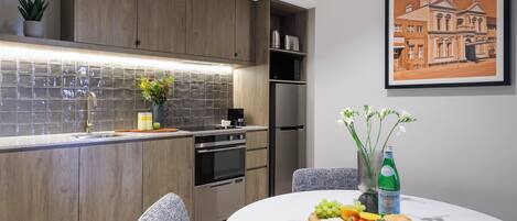 A modern kitchen with wooden cabinets, a tiled backsplash, stainless steel appliances, and a dining area with a marble table set for a meal.
