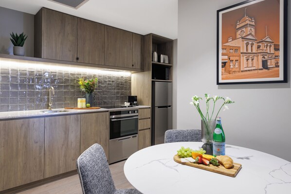 Una cocina moderna con armarios de madera, salpicadero de azulejos, electrodomésticos de acero inoxidable y un comedor con una mesa de mármol dispuesta para una comida.