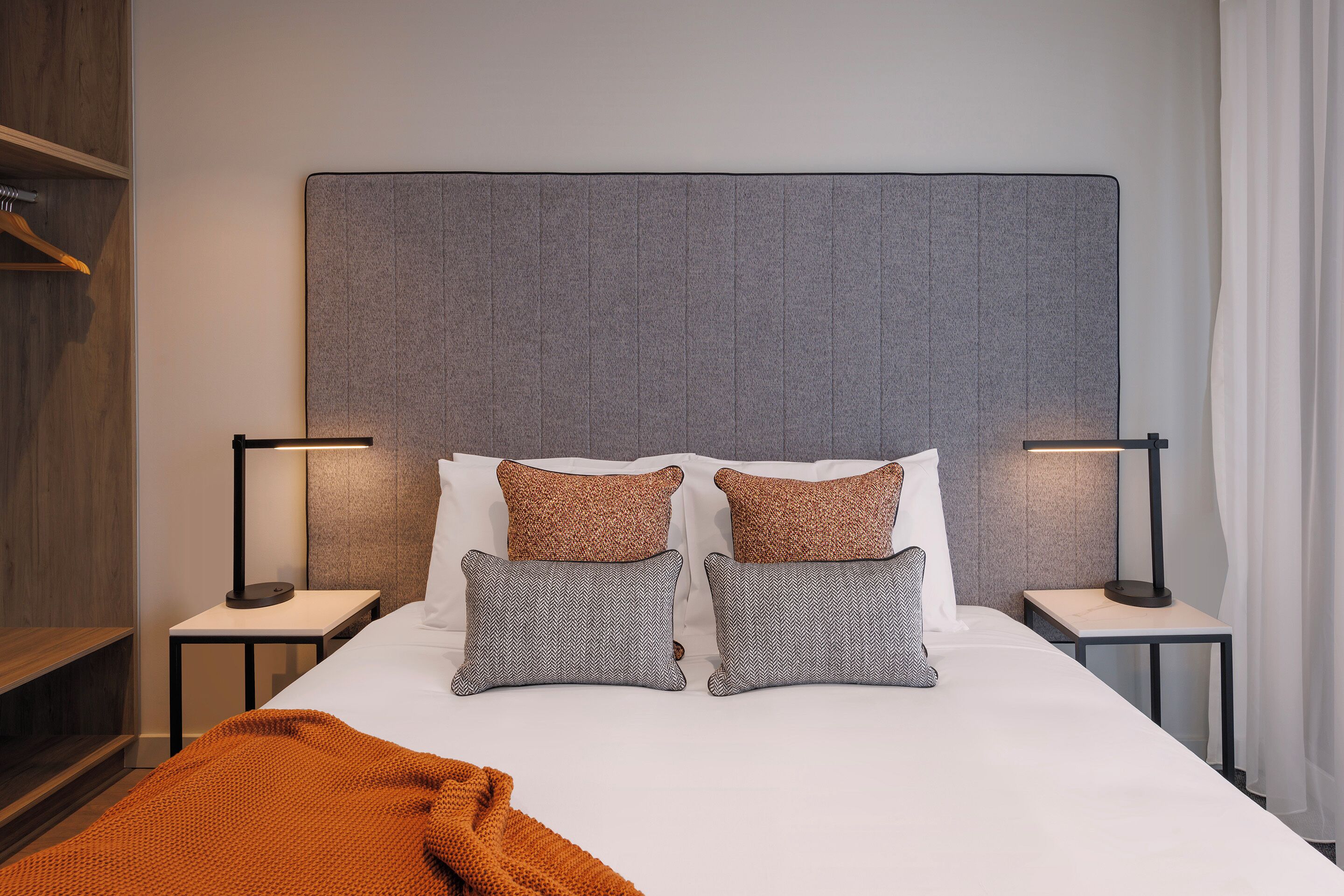 A neatly made bed with two pillows, two bedside tables with lamps, and a wooden shelf.