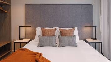 A neatly made bed with two pillows, two bedside tables with lamps, and a wooden shelf.