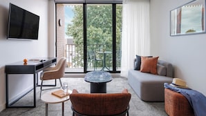 A modern room with a flat-screen TV, a desk, a comfortable sofa, a small round table, and a balcony with a view of trees and a building. - Punthill Maitland (Maitland)