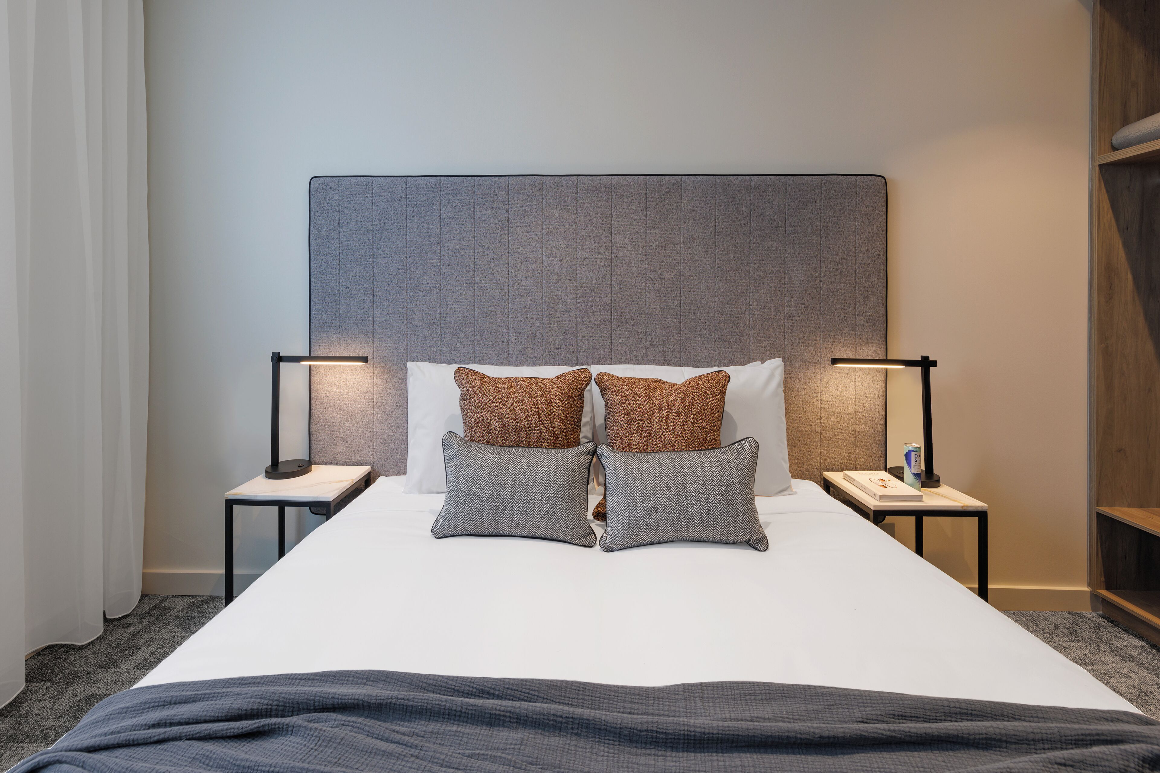 A neatly made bed with two pillows, two bedside tables with lamps, and a headboard.