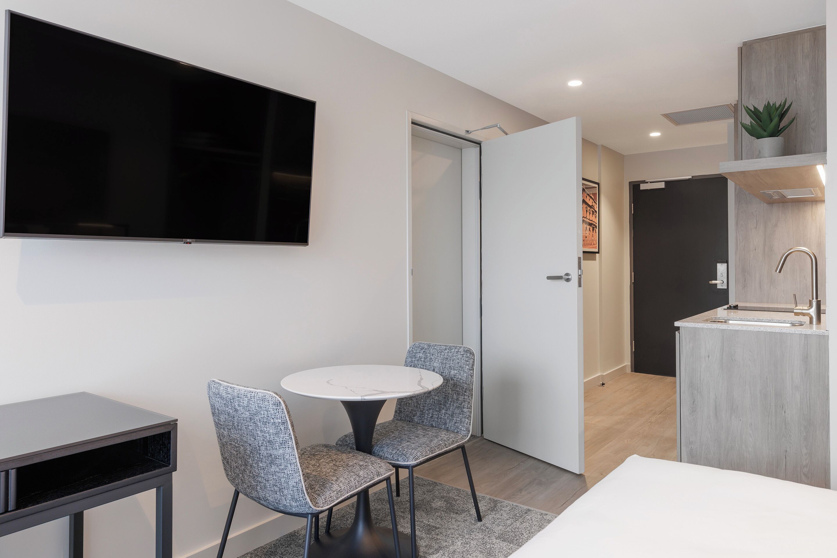 A modern kitchen with a built-in sink, a dining area with two chairs and a table, and a flat-screen TV mounted on the wall.