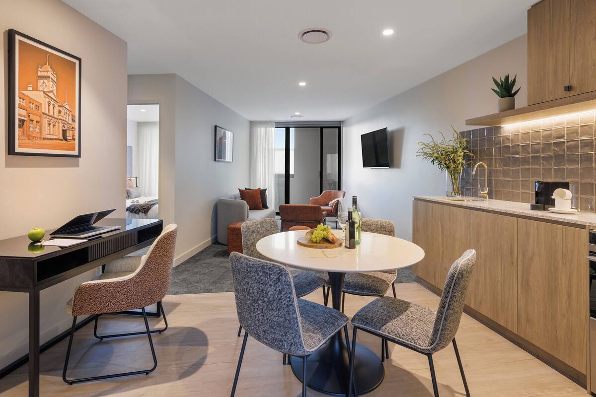 A modern kitchen with a round dining table, grey upholstered chairs, and a built-in oven.