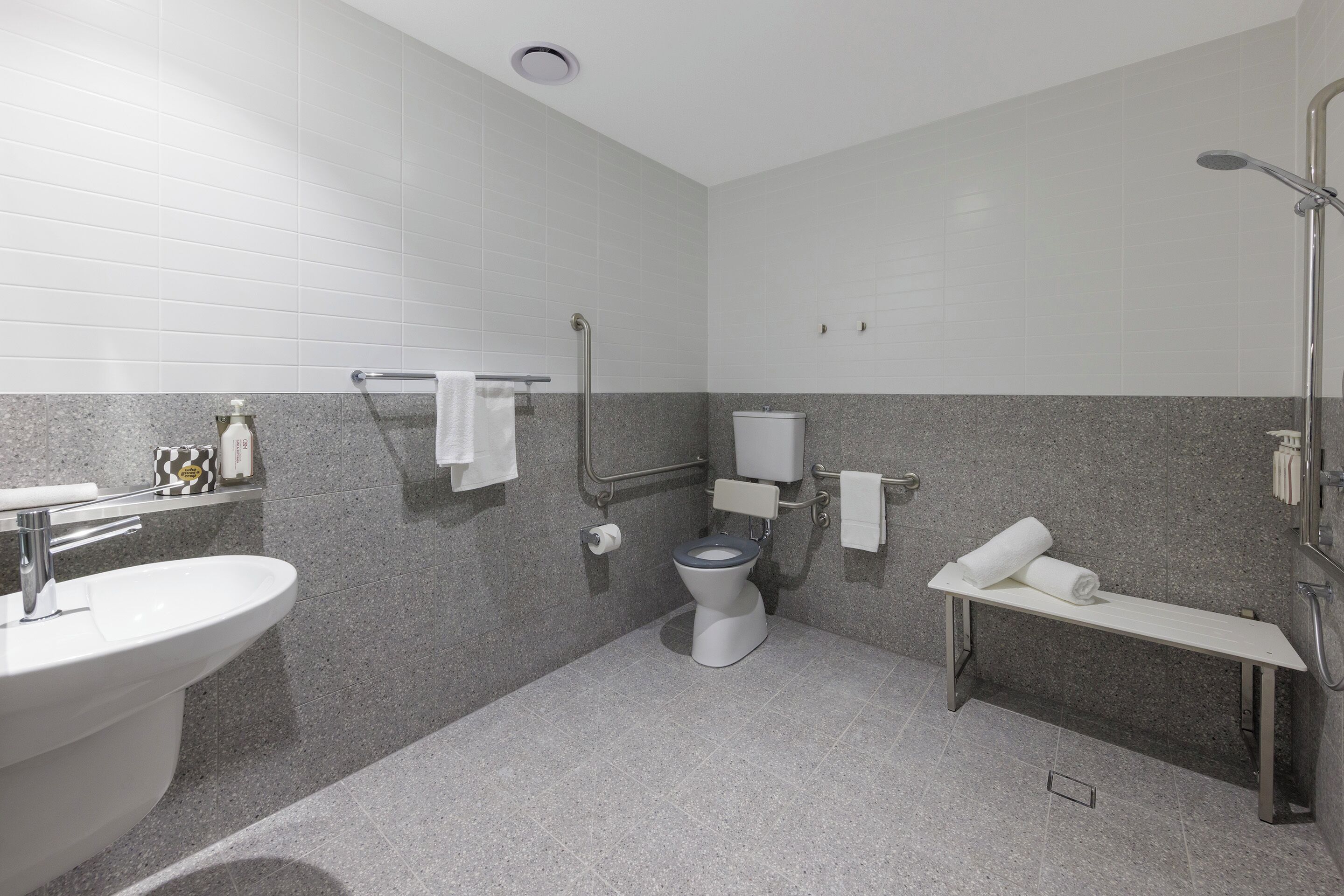 A modern bathroom with a white sink, toilet, and bench.