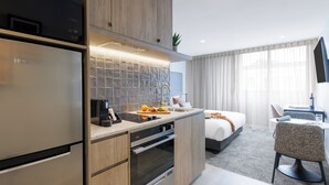 A modern kitchen with a built-in refrigerator, oven, and sink. There is a dining area with a table and chairs, and a bedroom with a bed and curtains. - Punthill Maitland (Maitland)