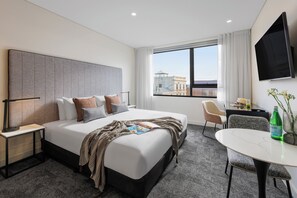 A modern hotel room with a large bed, a desk, a chair, a TV, and a window with a city view. - Punthill Maitland (Maitland)