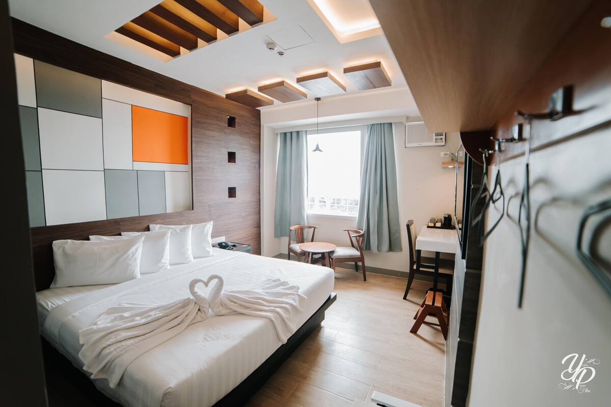A modern hotel room with a large bed, a dining area, and a view of the city.