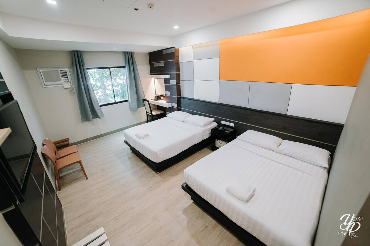 A hotel room with two beds, a desk, and a chair.