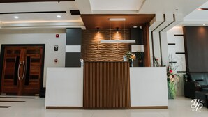 Una recepción con diseño moderno, que incluye un panel de madera y una barra blanca. Hay luces en el techo sobre la barra, y se ve una planta a la derecha.