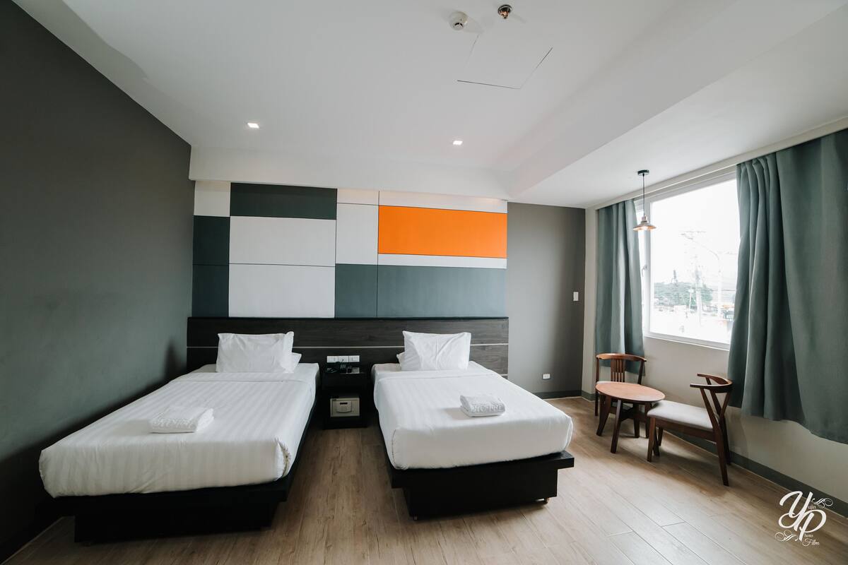 A hotel room with two beds, a small table, and a chair.