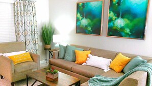 A living room with a sofa, armchairs, a coffee table, and two abstract paintings on the wall.