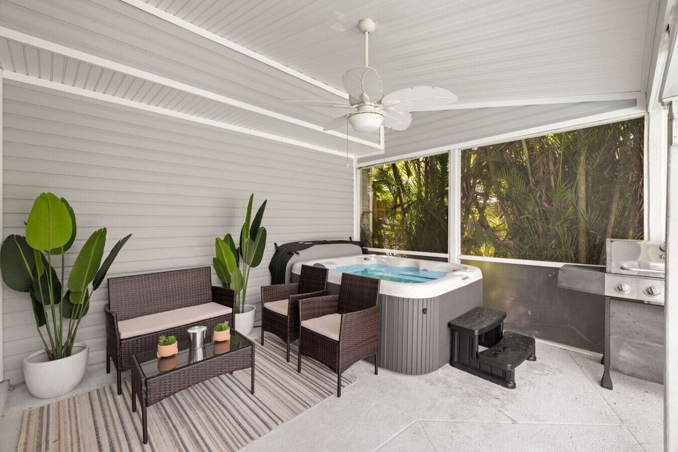 A covered outdoor area with wicker furniture, a hot tub, and a grill.