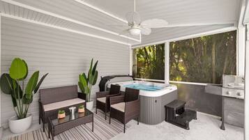 A covered outdoor area with wicker furniture, a hot tub, and a grill.