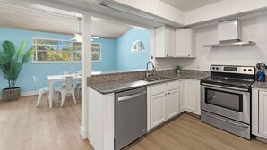 Une cuisine moderne avec des meubles blancs, un plan de travail en granit, des appareils en acier inoxydable et un coin repas comprenant une table et des chaises blanches.