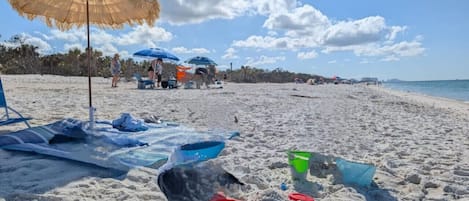 A beach with umbrellas, beach chairs, and sand toys.
