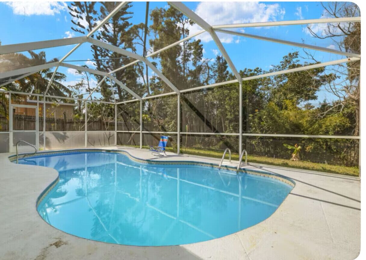 A swimming pool with a glass enclosure, surrounded by a fence and trees.