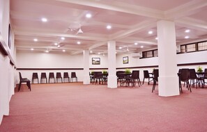 A spacious indoor area with rows of chairs and tables, ceiling fans, and recessed lighting.