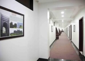 A hallway with framed pictures on the walls, a carpeted floor, and doors on the right side. - Hotel Pearls (Chhatrapati Sambhajinagar)