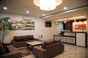 A hotel lobby with a reception desk, sofas, a coffee table, and wall-mounted air conditioning units. - Hotel Pearls (Chhatrapati Sambhajinagar)