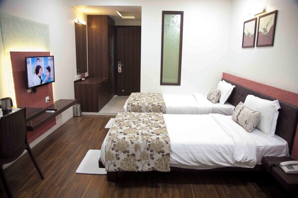 A hotel room with two beds, a desk, a TV, and a door leading to a bathroom.