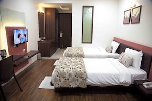 A hotel room with two beds, a desk, a TV, and a door leading to a bathroom. - Hotel Pearls (Chhatrapati Sambhajinagar)
