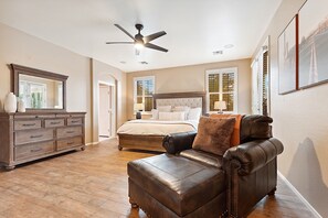 A bedroom with a bed, dresser, leather armchair, ceiling fan, and large windows. - Goodyear Springs * Private Pool & Community Playground (Goodyear)