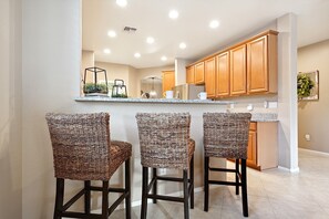 A kitchen with wooden cabinets, a granite countertop, and three wicker bar stools. - Goodyear Springs * Private Pool & Community Playground (Goodyear)