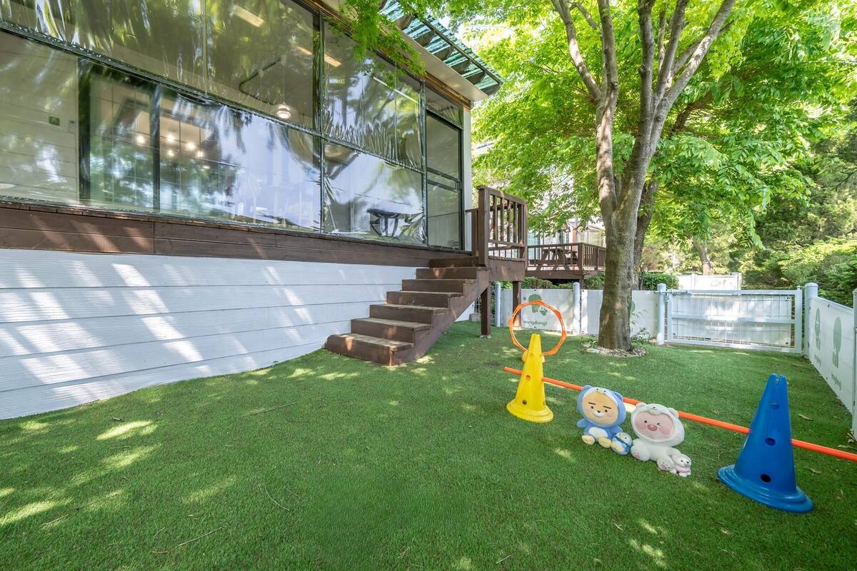 Propiedad residencial con terraza de madera, escalera que lleva a un porche cubierto y césped cuidado.