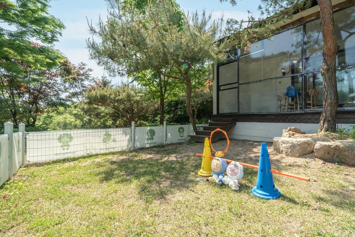 Un espacio exterior cercado con un área de juegos, que incluye un columpio amarillo y un cono azul.