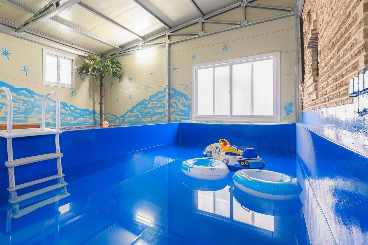 Una piscina interior con suelo azul, una escalera y dos aros inflables.