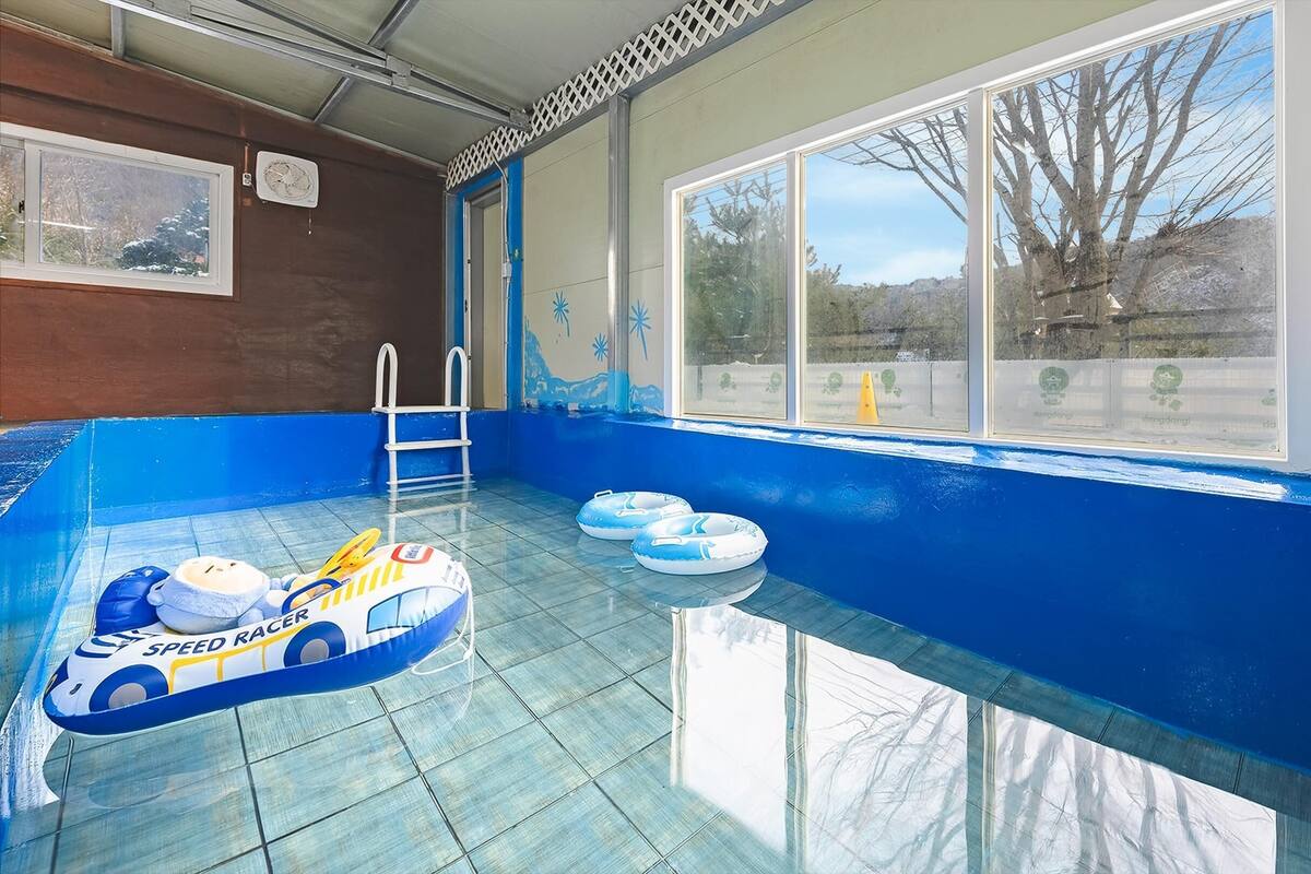 Una piscina interior con paredes azules, suelo de cristal transparente y juguetes inflables.