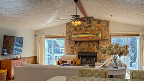 A cozy living room with a stone fireplace, a ceiling fan, and a large window.