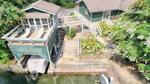 A house with a dock extending into a body of water, a covered boat, and a staircase leading to a deck.