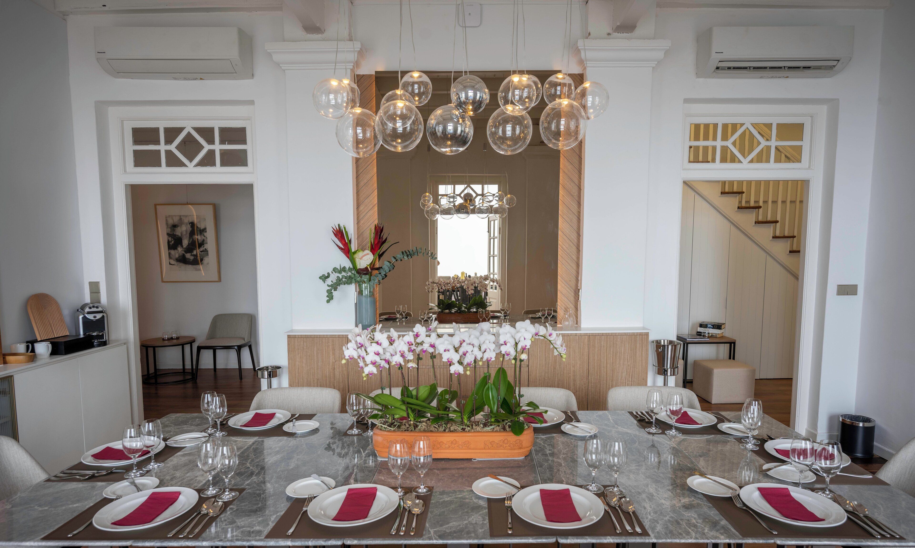 A dining area with a marble table set for a meal, surrounded by chairs, and a decorative orchid centerpiece.