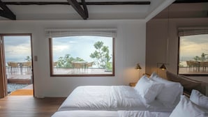 A bedroom with a large bed, a window with a view of outdoor furniture, and a door leading to an outdoor area. - Eythrope Boutique Villa (George Town)