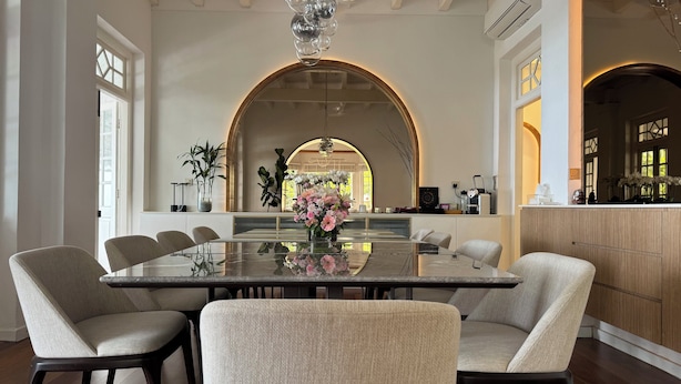 A spacious dining area with a large table surrounded by chairs, a decorative vase with flowers, and a view of the kitchen through an arched doorway. - Eythrope Boutique Villa (George Town)