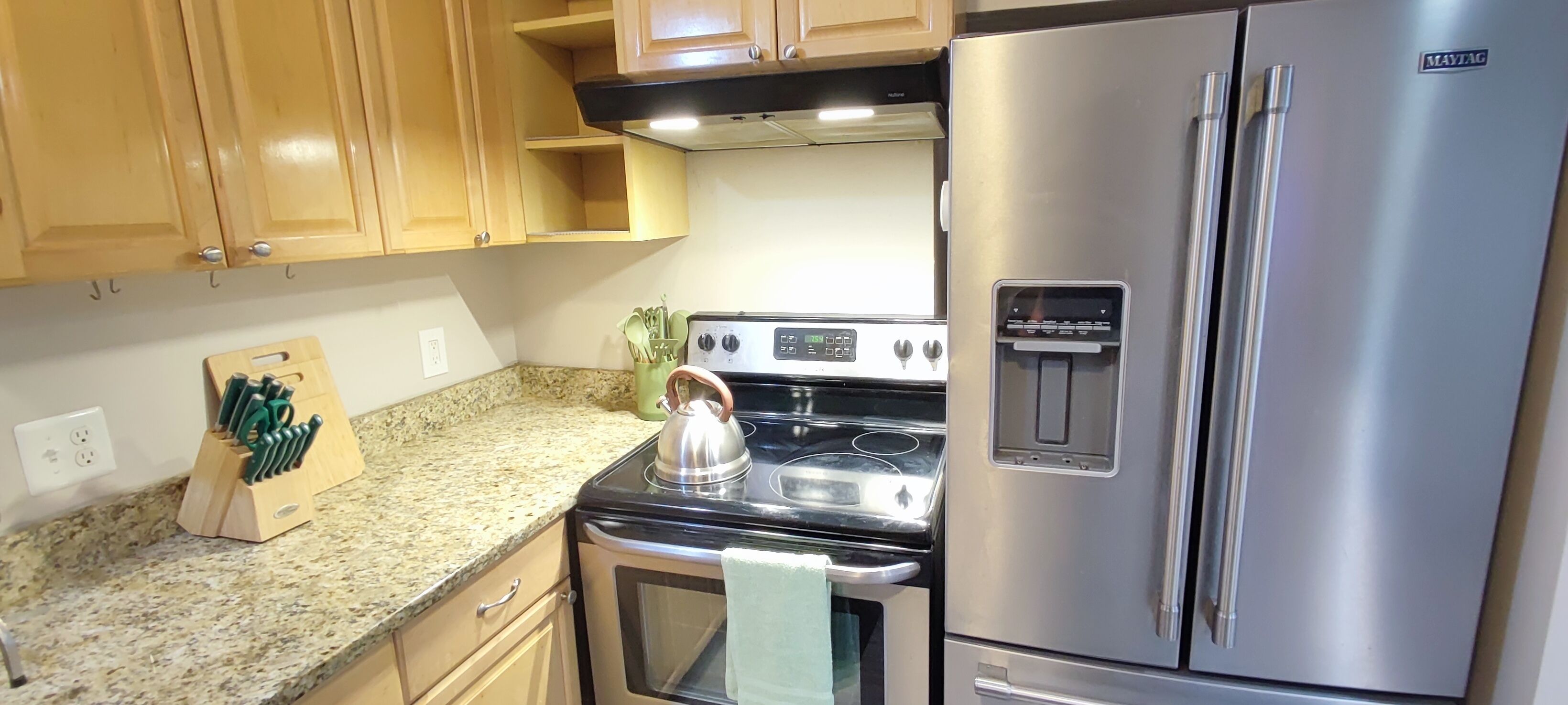 A kitchen with wooden cabinets, a stainless steel refrigerator, a stove, and a water dispenser.