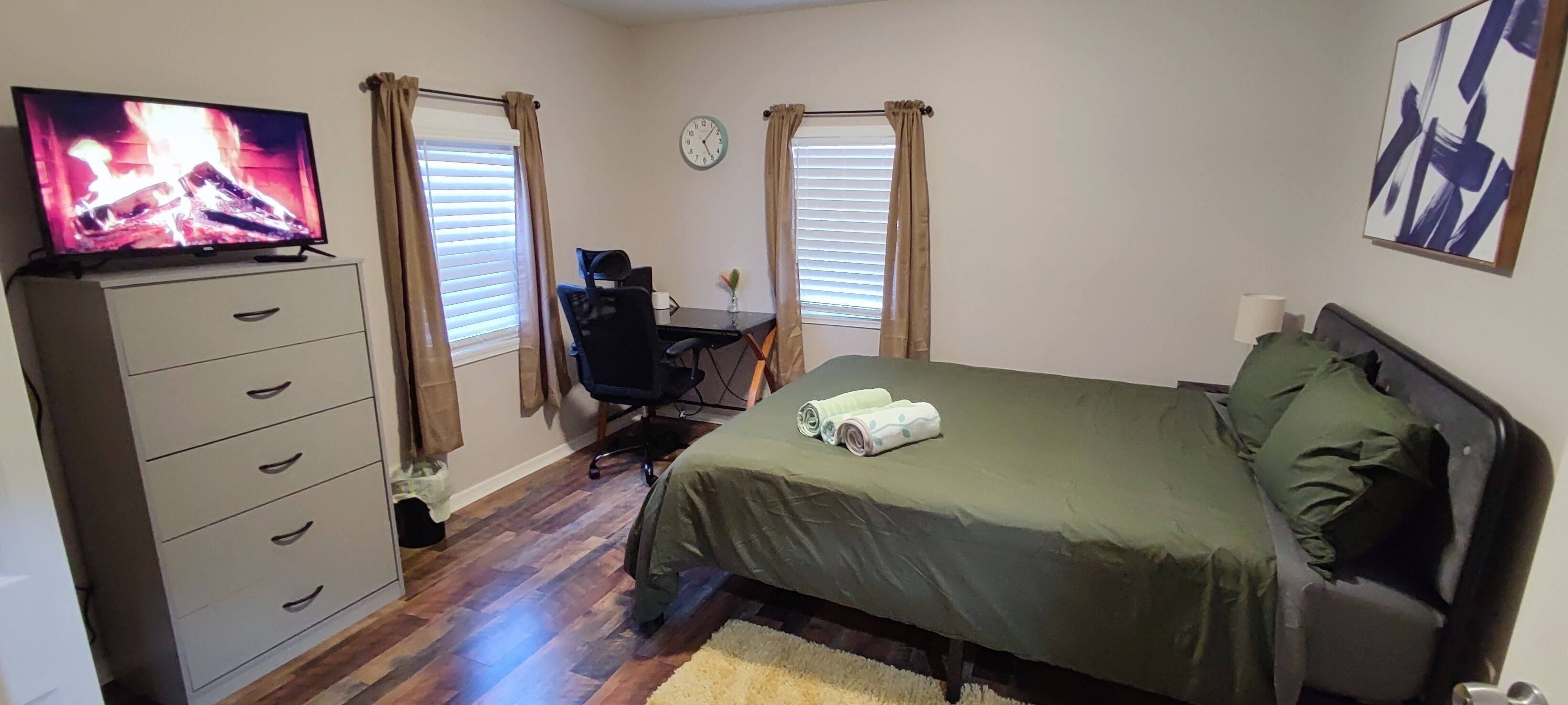 A bedroom with a bed, a desk, a chair, a TV, and a clock on the wall.