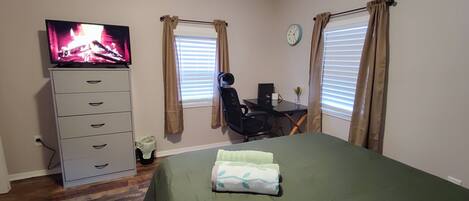 A bedroom with a bed, a desk with a chair, a television, and a dresser.