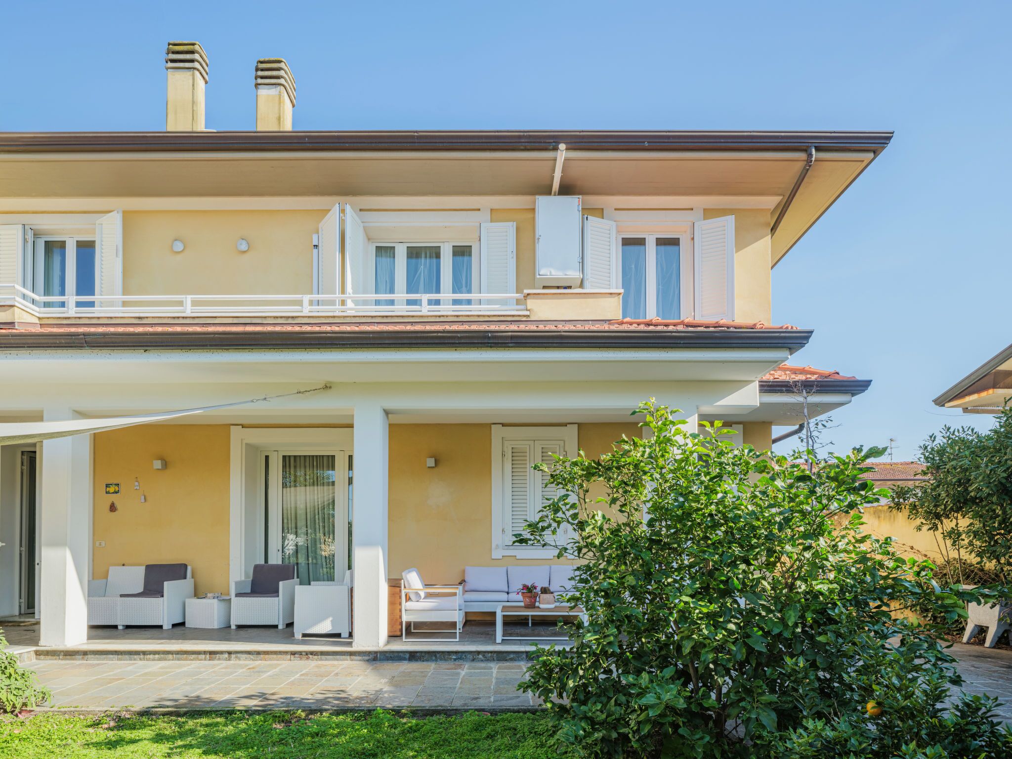 A two-story house with a balcony, a covered patio, and a garden area.