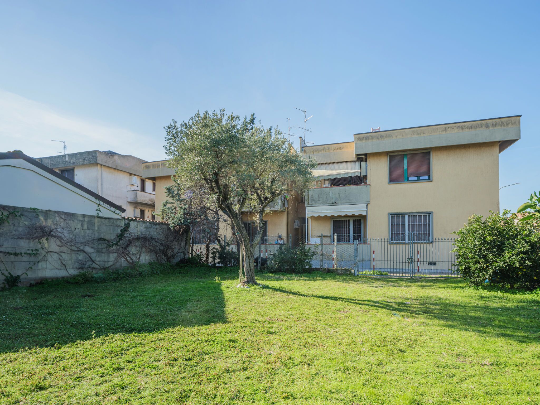 A residential building with a flat roof, a small garden, and a tree in the foreground.