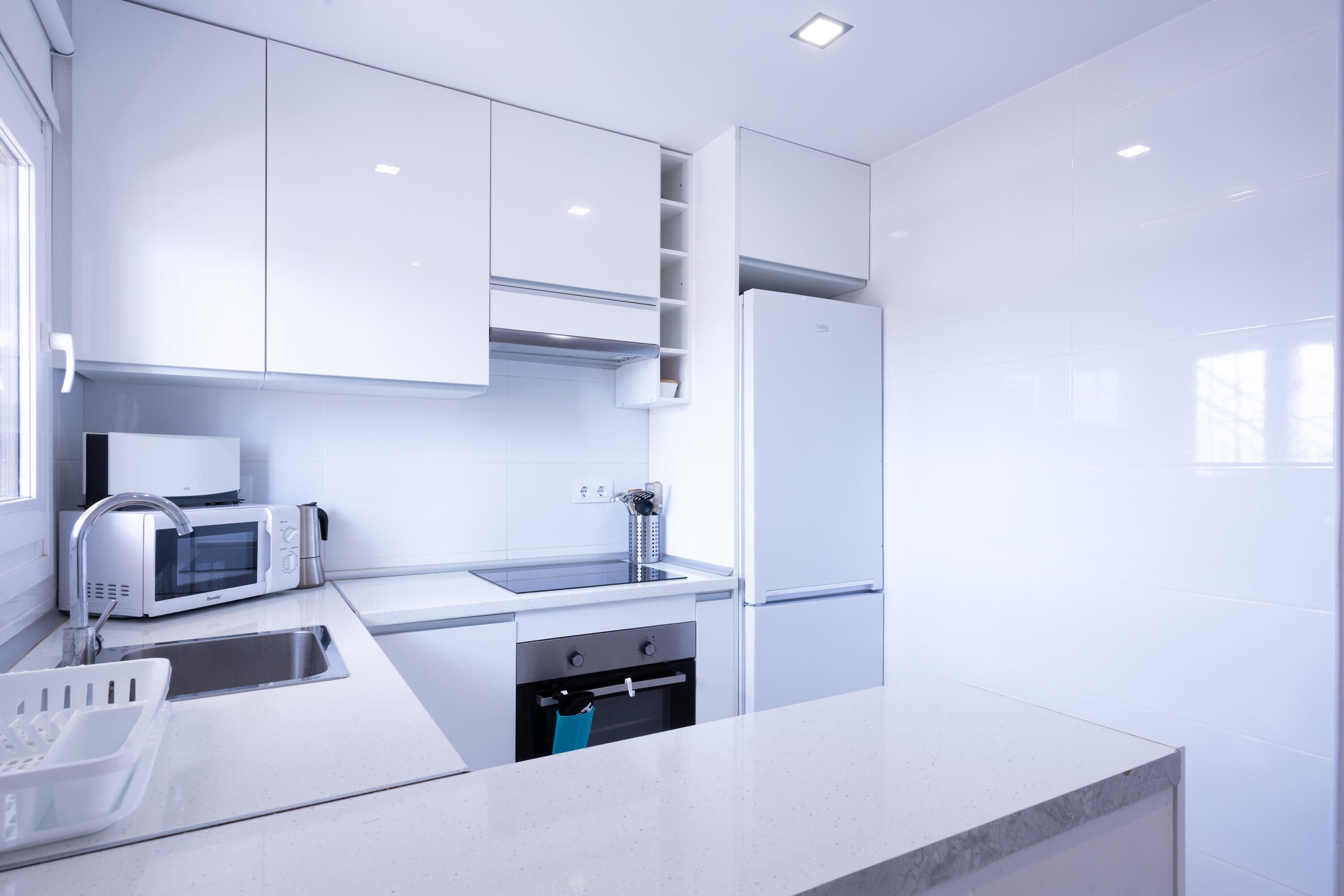 A modern kitchen with white cabinetry, a built-in microwave, a sink, and a stainless steel refrigerator.