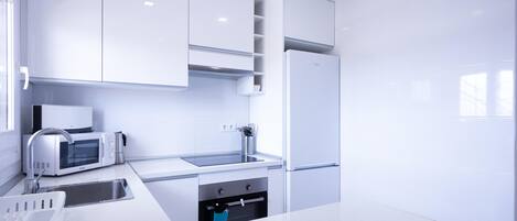 A modern kitchen with white cabinetry, a built-in microwave, a sink, and a stainless steel refrigerator.