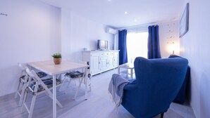 A modern living room with a dining table, blue armchair, white cabinet, and a TV.