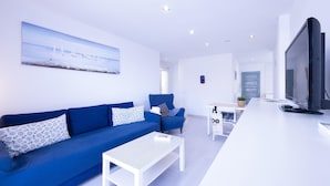 A modern living room with a blue sofa, a white coffee table, and a flat-screen TV.