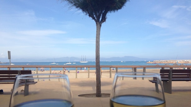 Two wine glasses on a table with a view of a beach and the sea.