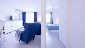 A modern hotel room with a white wardrobe, a blue armchair, a bed with a blue bedspread, and a ceiling fan.