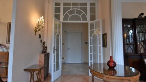 A hallway with a glass door leading to a room, a round table with a vase, and a cabinet with decorative items. - Aspromonte Garden House by Interhome (Milan)