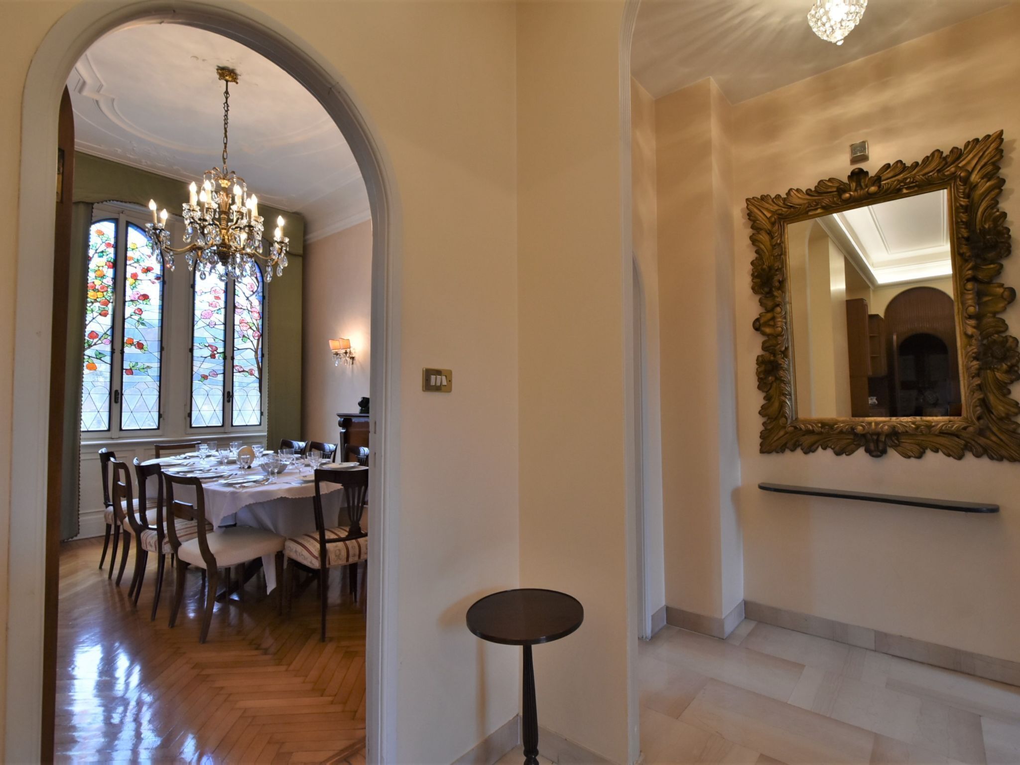 A dining area with a chandelier, stained glass windows, and a large ornate mirror on the wall.